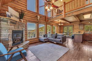Living room featuring rustic walls, a stone fireplace, french doors, ceiling fan, and hardwood / wood-style floors
