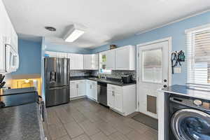 Kitchen with washer / clothes dryer, appliances with stainless steel finishes, white cabinets, dark countertops, and backsplash