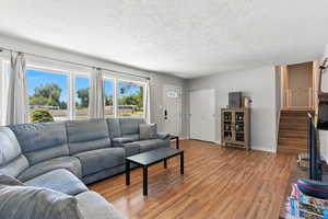 Living room featuring light wood-type flooring, a textured ceiling, and stairs