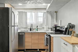 Kitchen featuring stainless steel appliances, light countertops, brown cabinetry, and a textured ceiling
