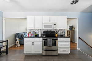 Kitchen featuring stainless steel range with electric cooktop, white microwave, dark countertops, decorative backsplash, and a textured ceiling