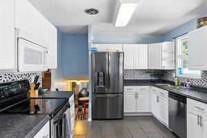 Kitchen with appliances with stainless steel finishes, dark countertops, white cabinetry, a textured ceiling, and backsplash