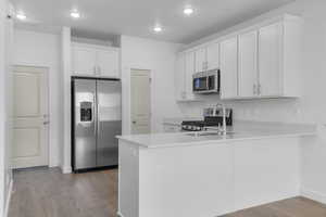 Kitchen with appliances with stainless steel finishes, a peninsula, wood finished floors, light countertops, and white cabinetry