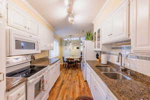 Kitchen featuring white appliances, white cabinets, light wood finished floors, decorative backsplash, and a textured ceiling