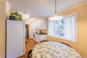 Kitchen with white appliances, white cabinetry, crown molding, light wood-type flooring, and dark countertops
