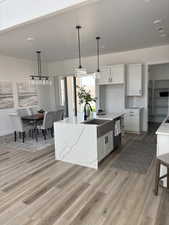 Kitchen with white cabinetry, hanging light fixtures, LVP floors, tasteful backsplash, and a kitchen island with sink