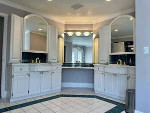 Elegant vanity in primary bath with decorative backsplash, two vanities, ornamental molding, tile patterned floors, and recessed lighting