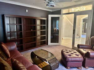 Carpeted den featuring ceiling fan, ornamental molding, and arched walkways and built in cabinets