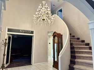 Grand staircase entry featuring tile patterned flooring, a towering ceiling, arched walkways, a chandelier, and a ceiling fan