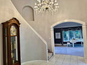 Staircase with carpet, tile patterned floors, a towering ceiling, and a chandelier