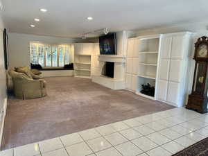Spacious family room featuring light carpet, ornamental molding, built in shelves, window seat, light tile patterned flooring, a fireplace, and recessed lighting