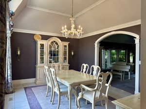 Dining space with arched walkways, a chandelier, light tile patterned floors, crown molding, and decorative columns