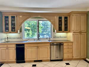 Kitchen with custom cabinetry, dishwasher, tasteful backsplash, light tile patterned floors, view of the lush back yard and crown molding