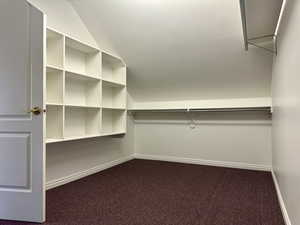 Spacious primary bedroom's closet featuring dark carpet and lofted ceiling