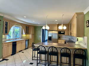 Kitchen with appliances with stainless steel finishes, designer etched glass insert cabinets, a peninsula, backsplash, and decorative light fixtures