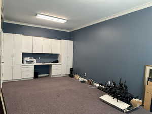 Unfurnished office with built in desk, carpet floors, and crown molding