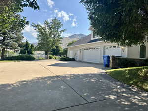 View of side of home with driveway, a mountain view, and a shingled roof