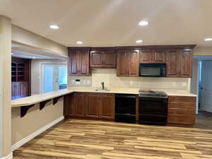 Kitchen with black appliances, light wood-style flooring, light countertops, recessed lighting, and dark brown cabinetry