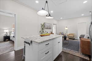 Kitchen featuring open floor plan, white cabinets, a center island, hanging light fixtures, and light stone countertops