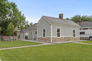 Rear view of house with stucco siding, a chimney, stone siding, and a shingled roof