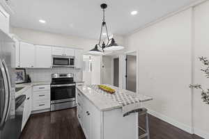 Kitchen with stainless steel appliances, tasteful backsplash, a center island, dark wood-style floors, and a kitchen breakfast bar