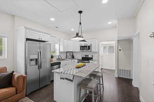 Kitchen with stainless steel appliances, backsplash, a center island, a kitchen breakfast bar, and dark wood-style floors