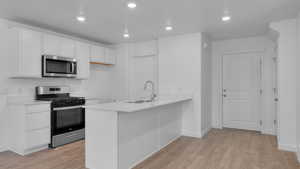 Kitchen with appliances with stainless steel finishes, light wood-style floors, white cabinetry, a peninsula, and light countertops