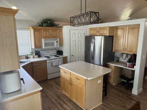 Kitchen featuring white appliances, dark wood finished floors, light countertops, a kitchen island, and a textured ceiling