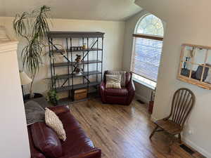 Sitting room with plenty of natural light, wood finished floors, lofted ceiling, and a textured ceiling