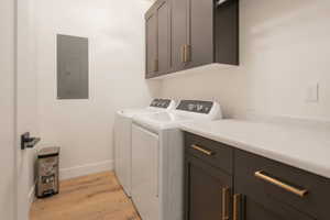 Washroom featuring cabinet space, washing machine and dryer, light wood-style flooring, and electric panel
