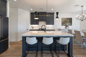 Kitchen with black fridge, a chandelier, light stone countertops, tasteful backsplash, and recessed lighting
