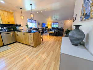 Kitchen with a peninsula, light brown cabinetry, light wood-type flooring, stainless steel dishwasher, and lofted ceiling