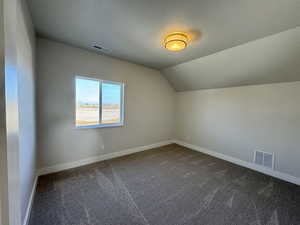 Bonus room with dark colored carpet, vaulted ceiling, and a textured ceiling