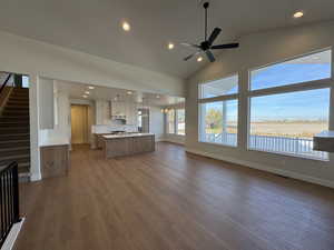 Unfurnished living room featuring recessed lighting, dark wood-style floors, high vaulted ceiling, ceiling fan, and a chandelier