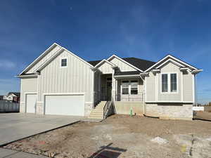 View of front facade featuring board and batten siding, stone siding, driveway, and a garage
