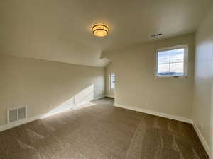 Carpeted empty room with plenty of natural light and vaulted ceiling