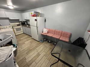 Kitchen featuring white appliances, wood tiled floors, washer / clothes dryer, under cabinet range hood, and white cabinets