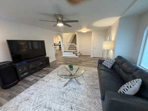 Living room with arched walkways, stairway, wood finished floors, and a ceiling fan