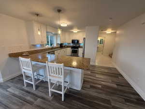 Kitchen with a peninsula, white cabinetry, appliances with stainless steel finishes, a kitchen bar, and dark wood-style flooring