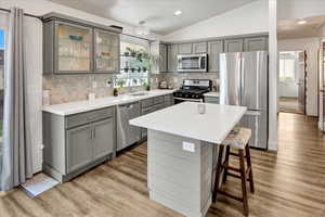 Kitchen with gray cabinetry, appliances with stainless steel finishes, lofted ceiling, light wood-type flooring, and recessed lighting