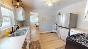 Kitchen with stainless steel appliances, a ceiling fan, light wood-type flooring, white cabinetry, and decorative light fixtures