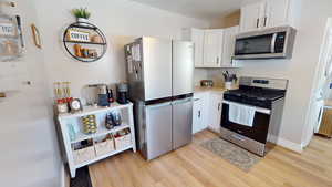 Kitchen featuring appliances with stainless steel finishes, light wood-type flooring, white cabinets, and light countertops