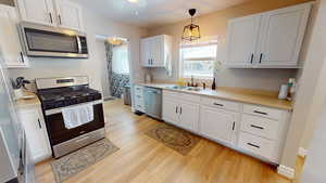 Kitchen with appliances with stainless steel finishes, light wood-type flooring, white cabinetry, and light countertops