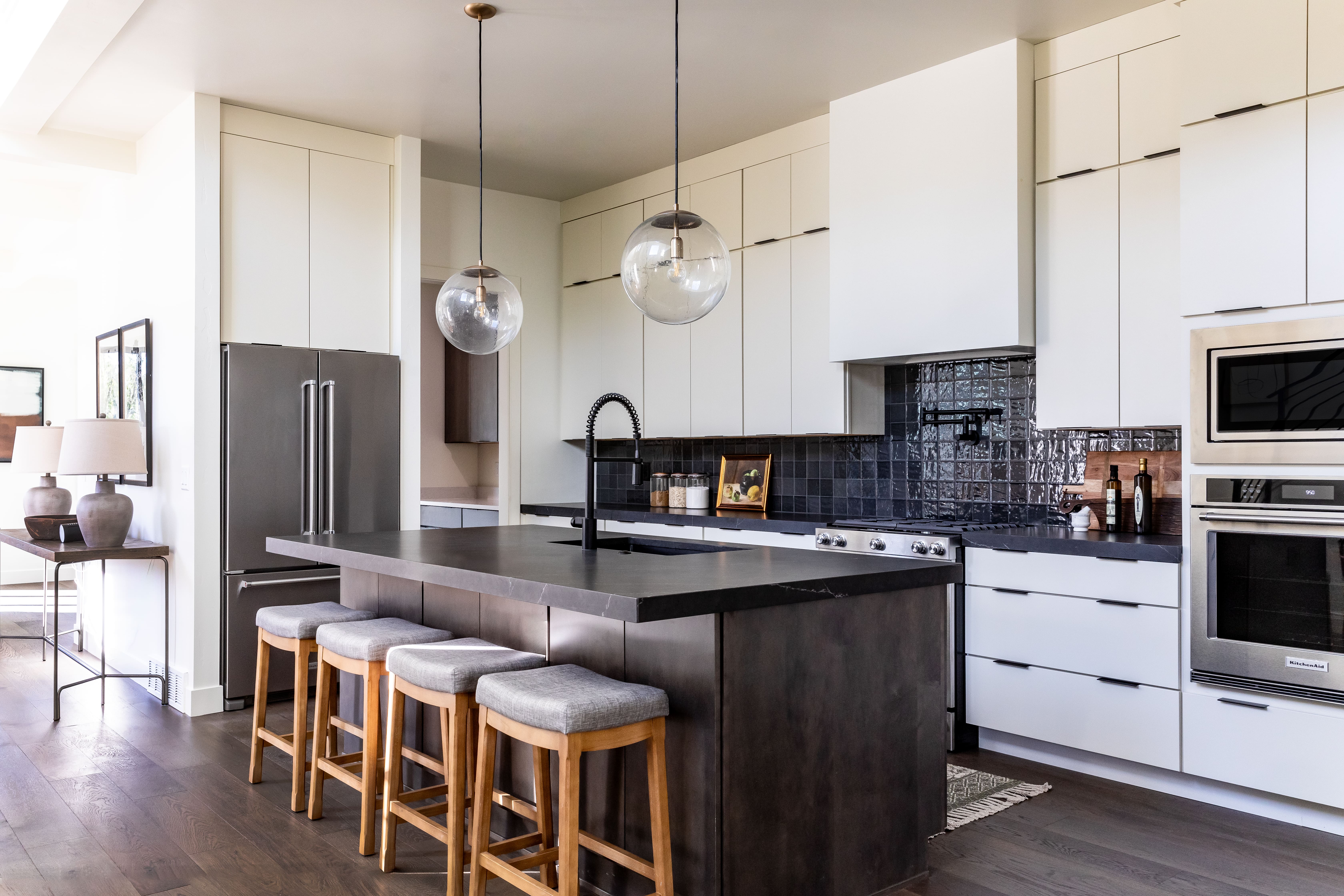 Kitchen featuring dark countertops, modern cabinets, dark wood-style flooring, appliances with stainless steel finishes, and tasteful backsplash