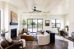 Living area with dark wood-type flooring, a ceiling fan, a fireplace, and beamed ceiling