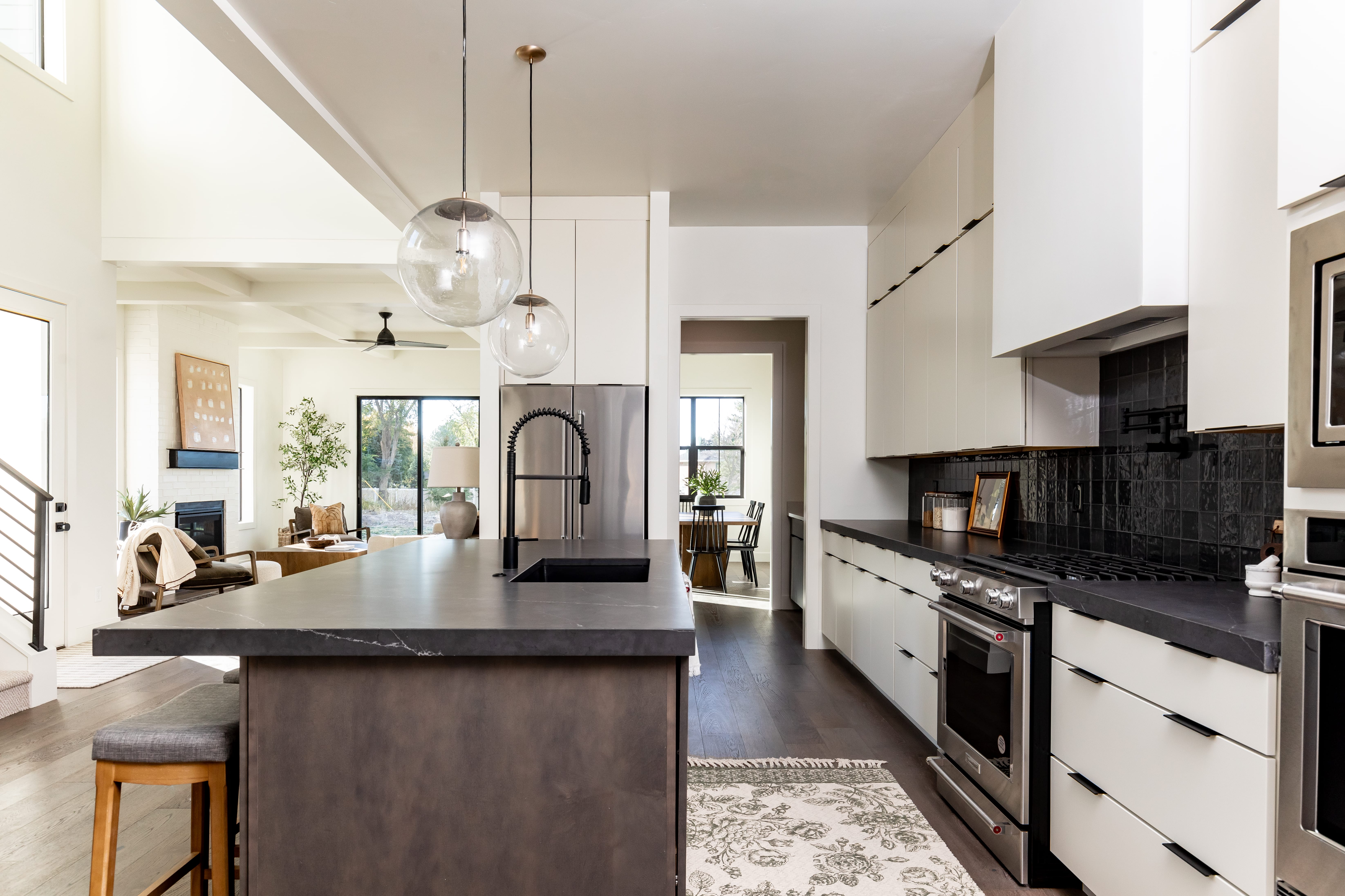 Kitchen with dark countertops, modern cabinets, a glass covered fireplace, stainless steel appliances, and beamed ceiling