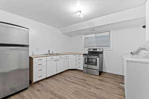 Kitchen featuring independent washer and dryer, fridge, stainless steel range with electric stovetop, and light wood finished floors