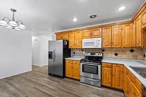 Kitchen featuring stainless steel appliances, a chandelier, tasteful backsplash, brown cabinets, and recessed lighting