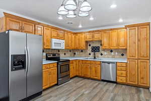 Kitchen featuring appliances with stainless steel finishes, light countertops, light wood-style floors, a chandelier, and decorative backsplash
