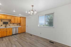 Kitchen featuring light countertops, tasteful backsplash, wood finished floors, stainless steel dishwasher, and a chandelier